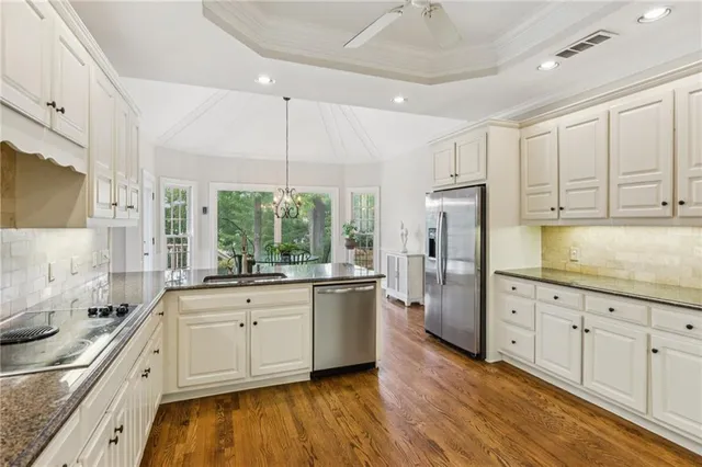 a kitchen with stainless steel appliances granite countertop a stove a sink dishwasher a refrigerator and white cabinets with wooden floor