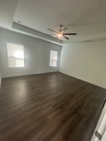 an empty room with wooden floor chandelier fan and windows
