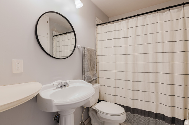 244 North 600 West Logan, UT 84321 - Photo 11 of 30 Pedestal sink with a dual-handle chrome faucet, round black-framed mirror, and wall-mounted light fixture