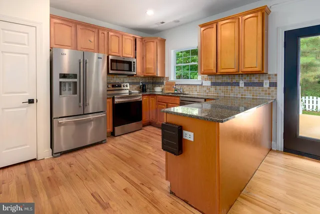 a kitchen with granite countertop wooden floors stainless steel appliances a window and a counter space