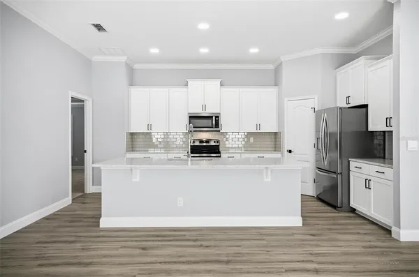 a large kitchen with stainless steel appliances a refrigerator stove and white cabinets