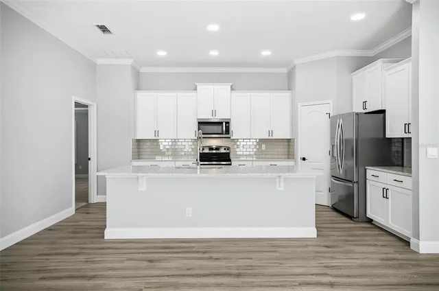 a large kitchen with stainless steel appliances a refrigerator stove and white cabinets