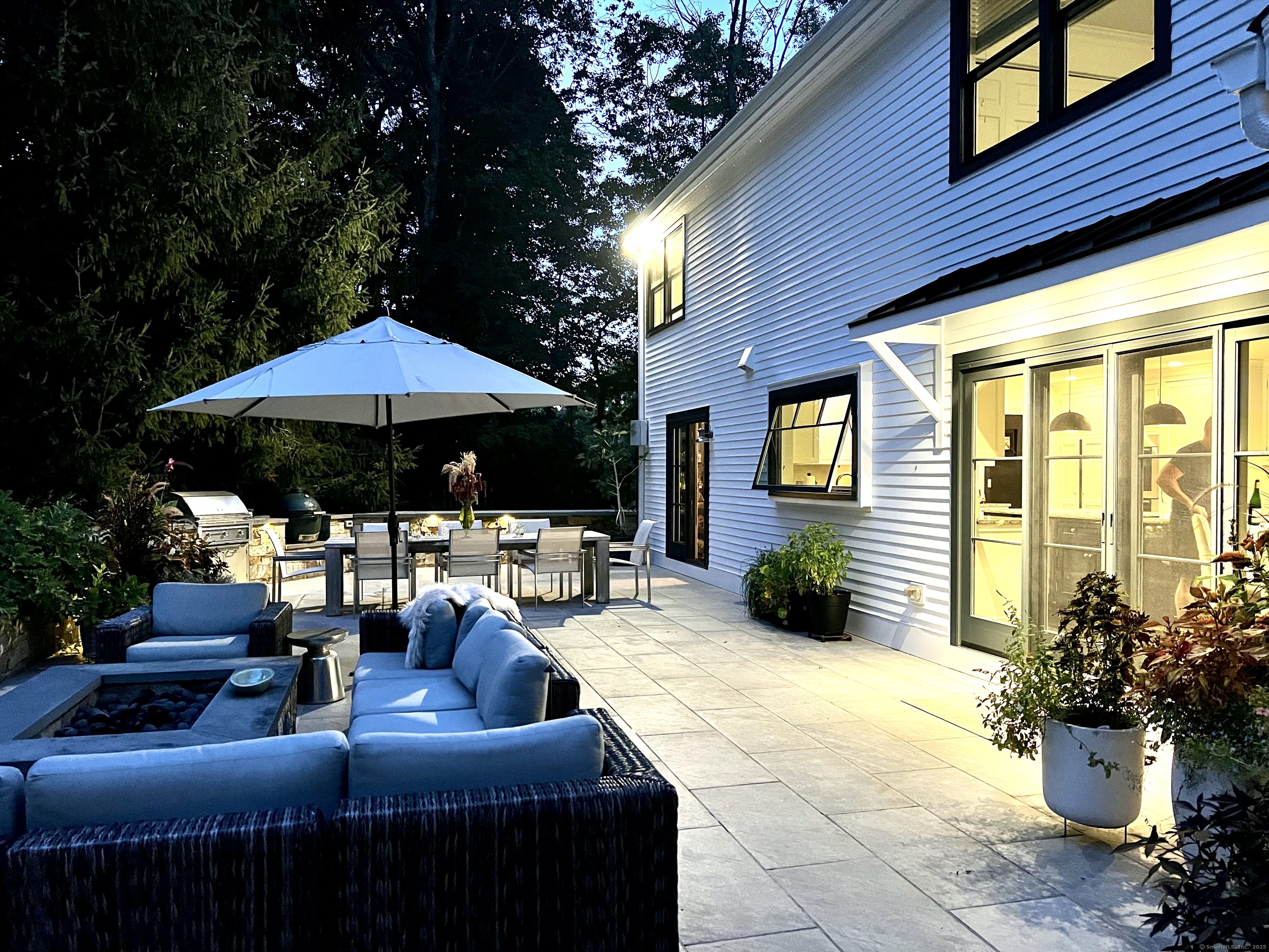 81 Graenest Ridge Road Wilton, CT 06897 - Photo 35 of 39 a view of a patio with couches table and chairs under an umbrella with a fire pit and potted plants