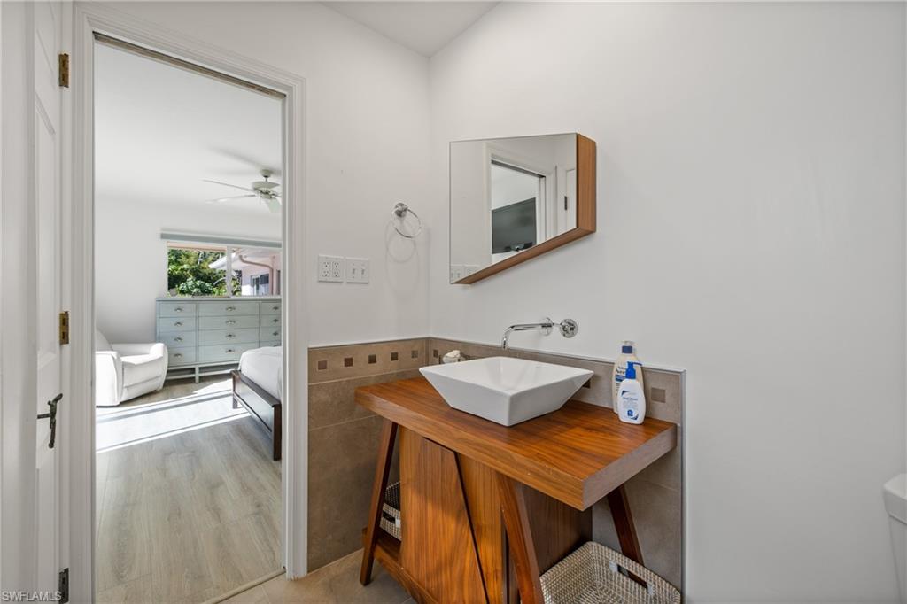 540 Rudder Road Naples, FL 34102 - Photo 36 of 37 Bathroom featuring tile walls, connected bathroom, wood finished floors, vanity, and a ceiling fan