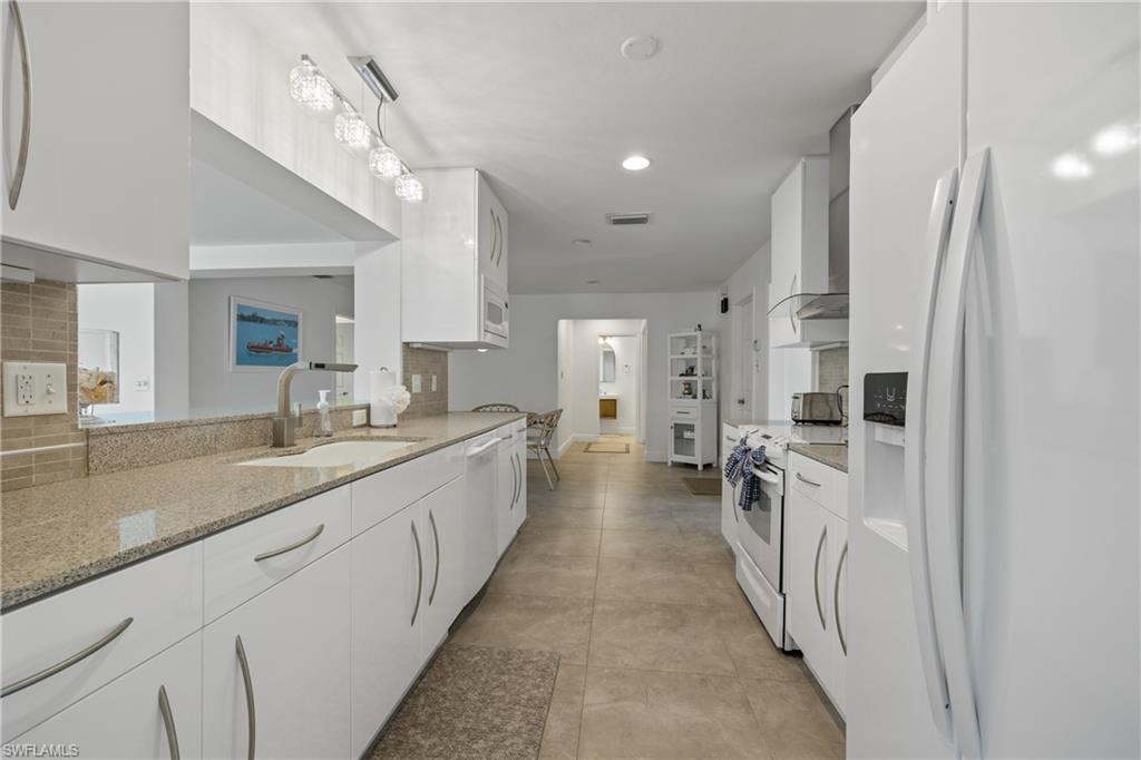 540 Rudder Road Naples, FL 34102 - Photo 5 of 37 Kitchen featuring white cabinetry, white appliances, backsplash, a sink, and light stone countertops
