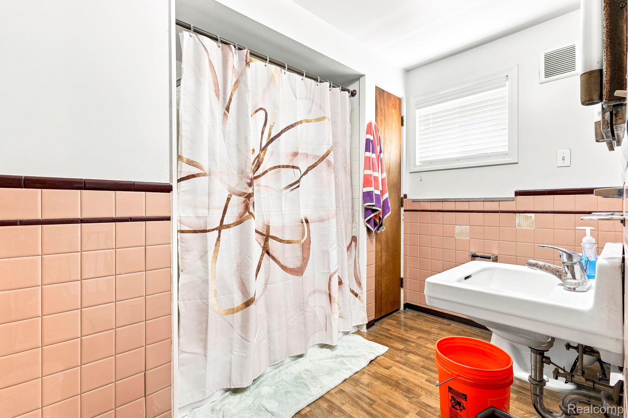 9735 Dolan Road Columbus, MI 48063 - Photo 37 of 63 Bathroom featuring a white wall-mounted sink, warm-toned wall tiles with a contrasting trim, and wood-finish flooring