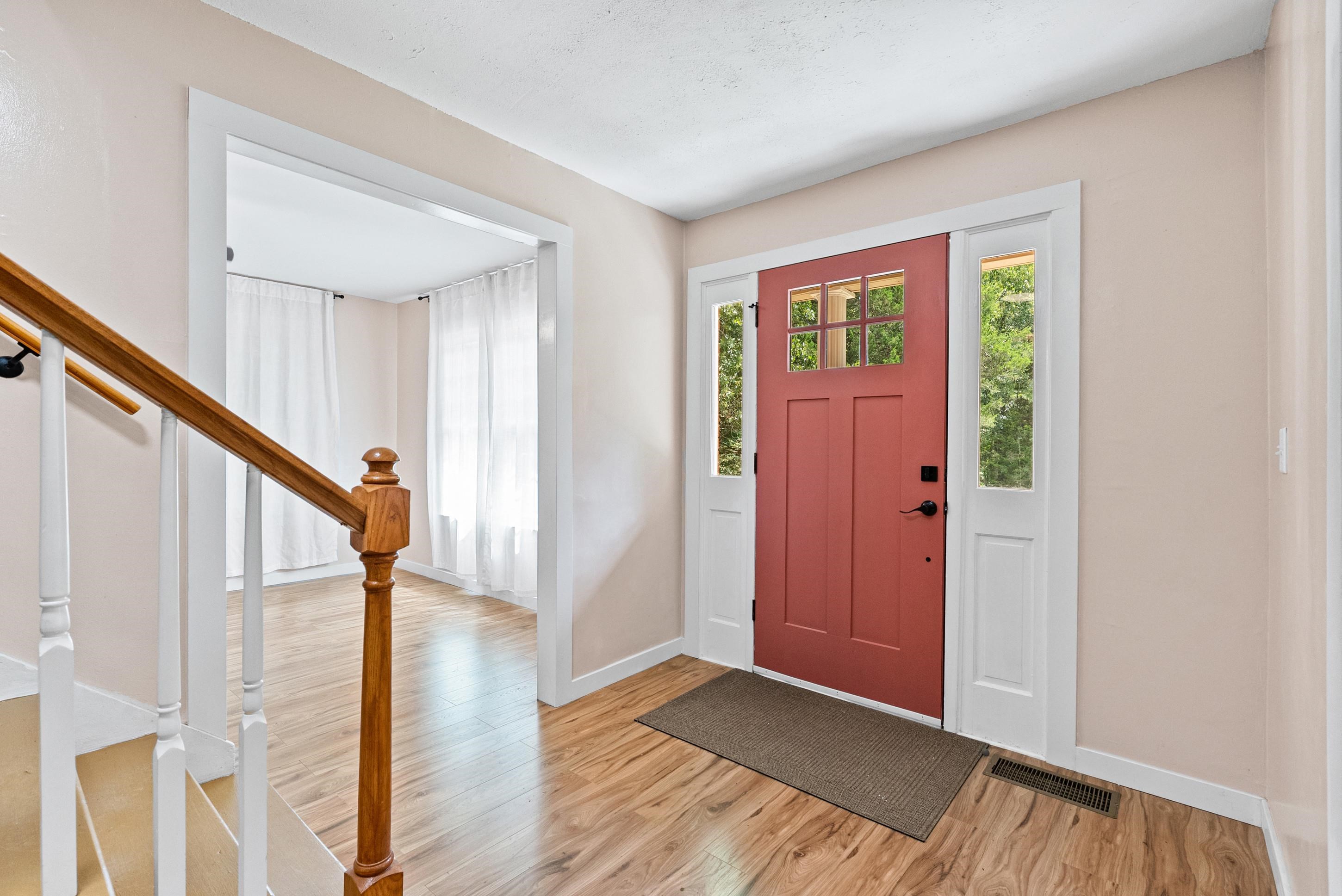 779 Strickland Road Coldwater, MS 38618 - Photo 5 of 40 Wood-finish flooring throughout, solid wood staircase with white risers, and a red front door with clear glass panels