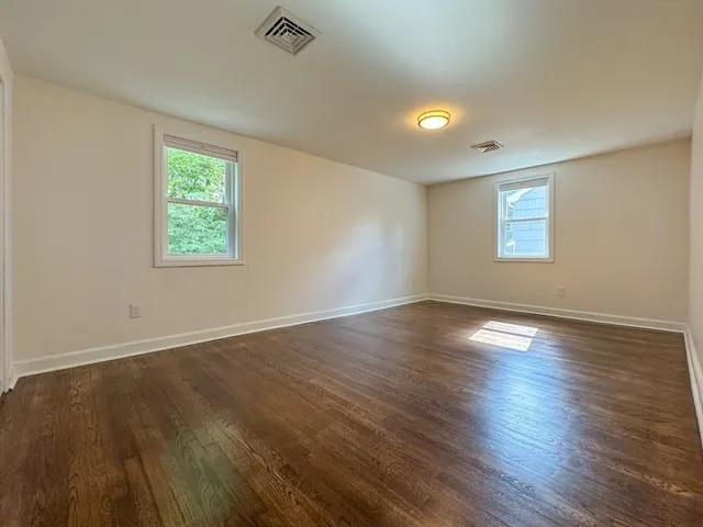 a view of an empty room with wooden floor and window