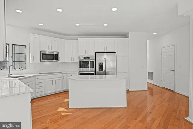 a kitchen with stainless steel appliances granite countertop a stove a sink and white cabinets with wooden floor