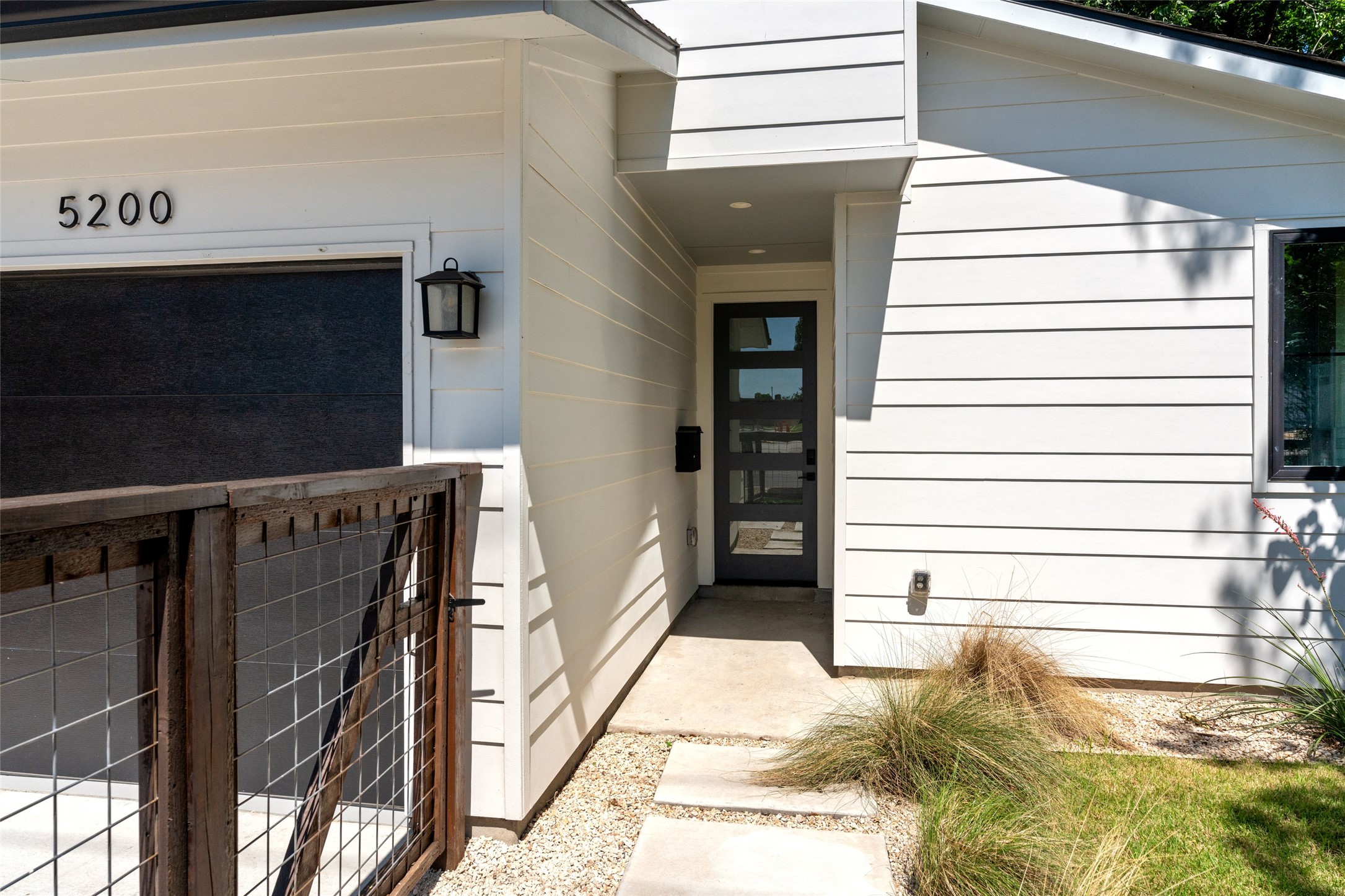 5200 Grover Avenue Austin, TX 78756 - Photo 5 of 32 Contemporary white siding exterior featuring a dark paneled front door, an integrated garage, a concrete walkway, and a decorative wire-mesh gate.