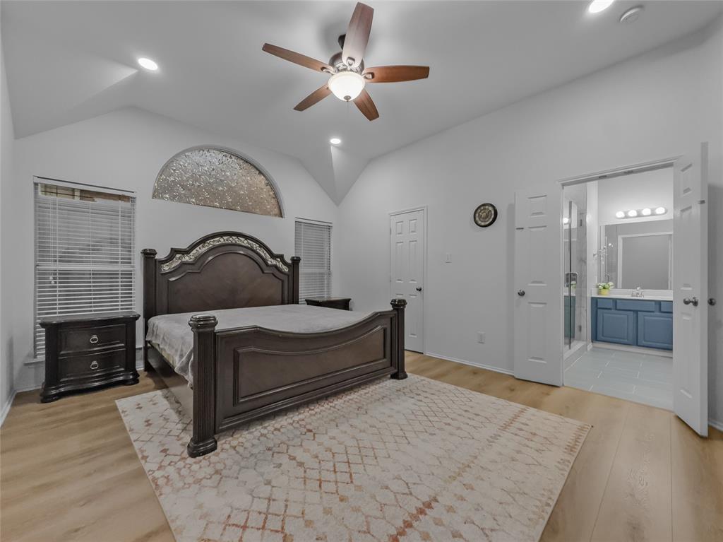 3008 Devlin Ridge Drive Plano, TX 75025 - Photo 12 of 24 Vaulted ceiling bedroom featuring recessed lighting, a ceiling fan, a decorative arched window, wood-finish flooring, and a full bathroom with a walk-in shower and a vanity with a blue base cabinet