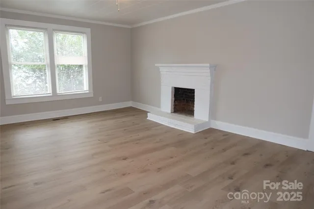 an empty room with wooden floor fireplace and windows