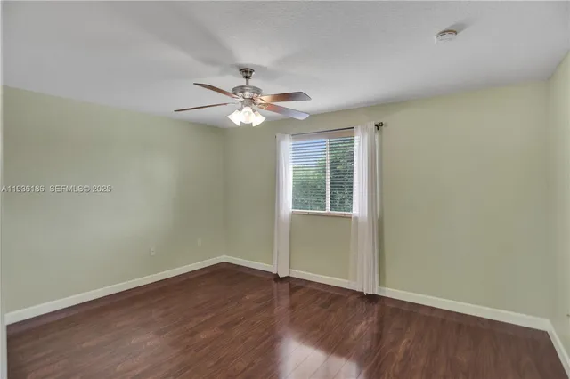 an empty room with wooden floor fan and windows