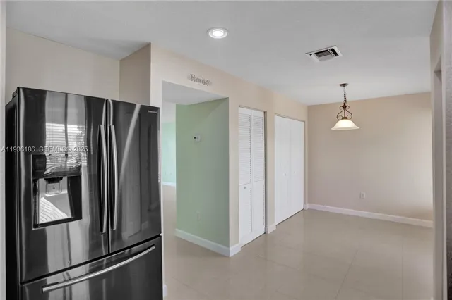 a view of a refrigerator in kitchen and an empty room with wooden floor windows