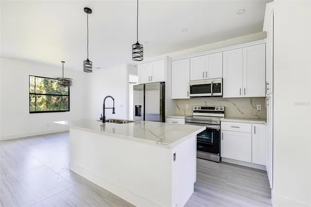 a kitchen with stainless steel appliances granite countertop a sink a stove a refrigerator cabinets and a wooden floor