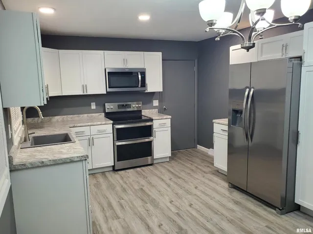 a kitchen with stainless steel appliances granite countertop white cabinets a refrigerator a stove a sink and a microwave