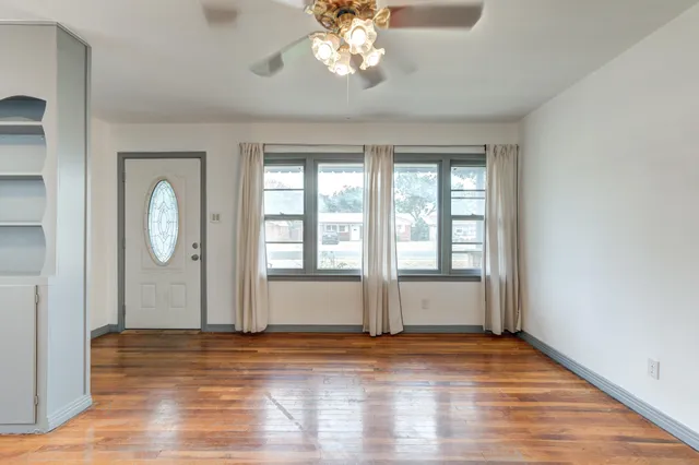 a view of an empty room with wooden floor and fan