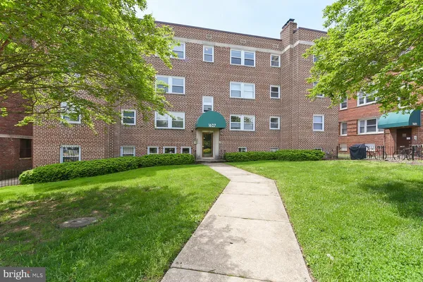 a view of a brick building next to a big yard and large trees