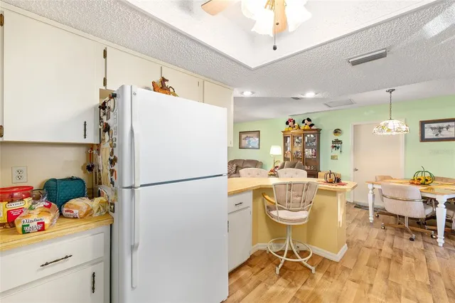 a white kitchen with a refrigerator a stove a dining table and chairs with wooden floor