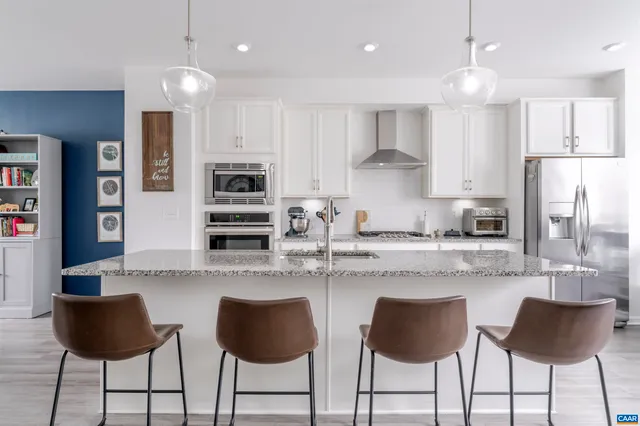 a kitchen with stainless steel appliances granite countertop a stove top oven a refrigerator a sink and a dining table with white cabinets