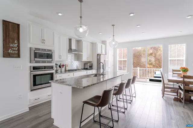 a kitchen with stainless steel appliances granite countertop a stove top oven a refrigerator a sink and a dining table with wooden floor