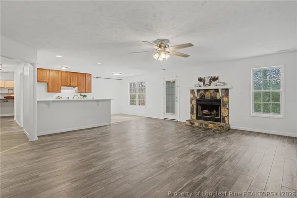 a view of a livingroom with a fireplace a ceiling fan and wooden floor