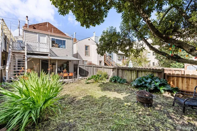 a backyard of a house with table and chairs potted plants and a large tree