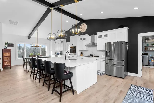 a kitchen with stainless steel appliances a refrigerator a stove a sink a dining table and chairs with wooden floor