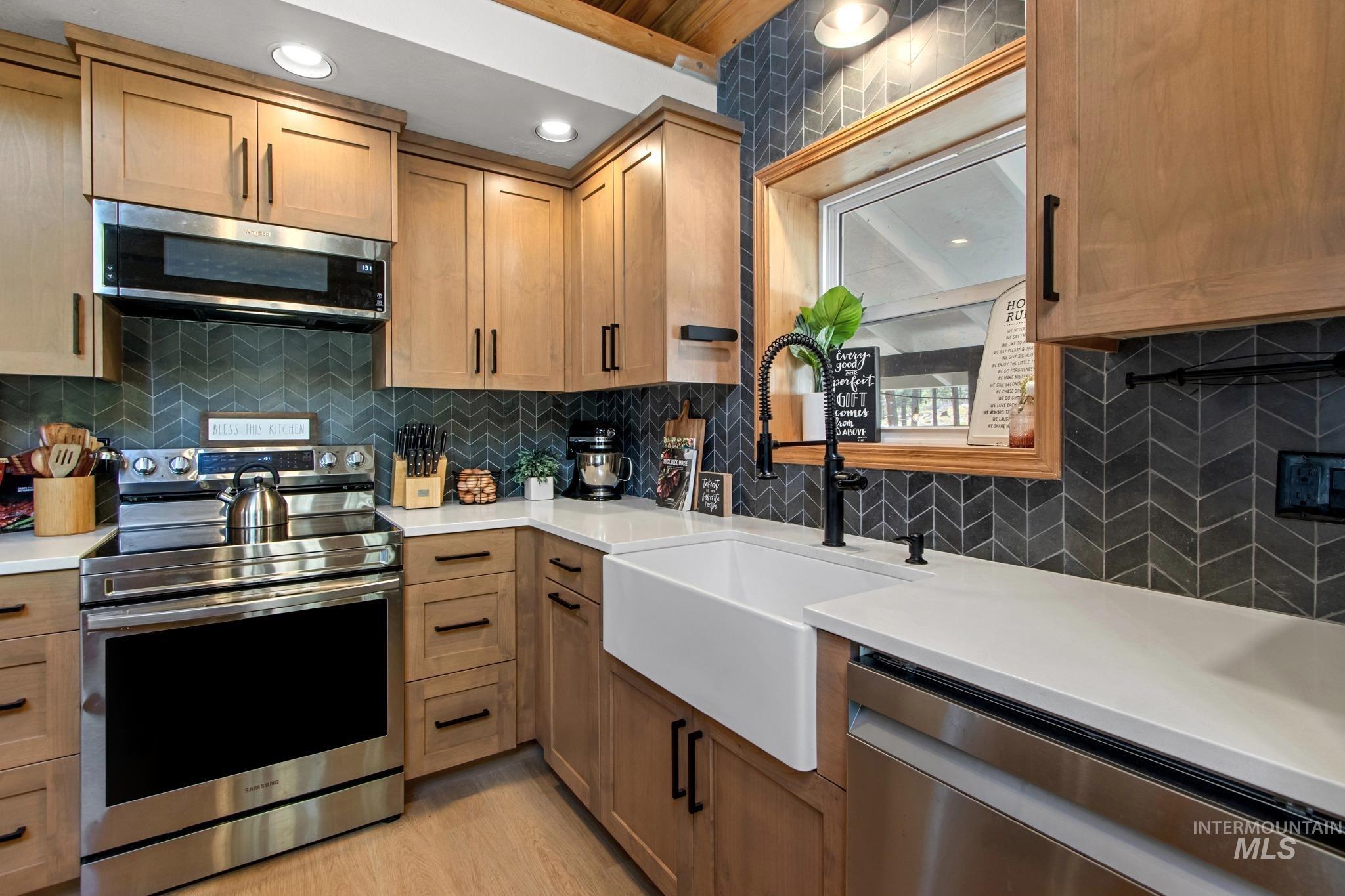 12 Meadow Creek Road Idaho City, ID 83631 - Photo 10 of 44 Kitchen featuring appliances with stainless steel finishes, backsplash, light wood finished floors, brown cabinets, and light stone counters