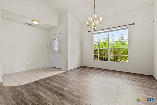an empty room with wooden floor chandelier and windows