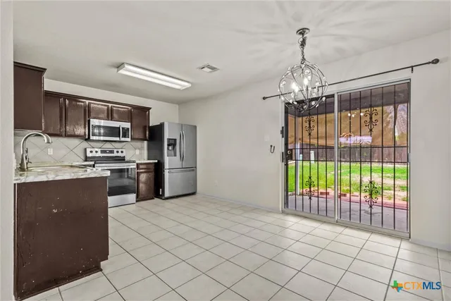 a kitchen with granite countertop stainless steel appliances a stove top oven a sink and a chandelier