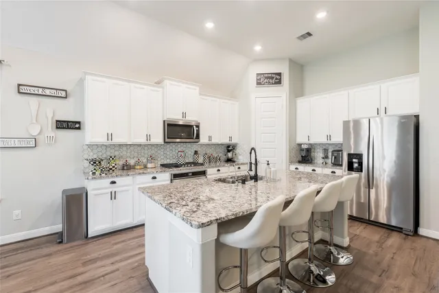 a kitchen with stainless steel appliances granite countertop a kitchen island hardwood floor and a refrigerator