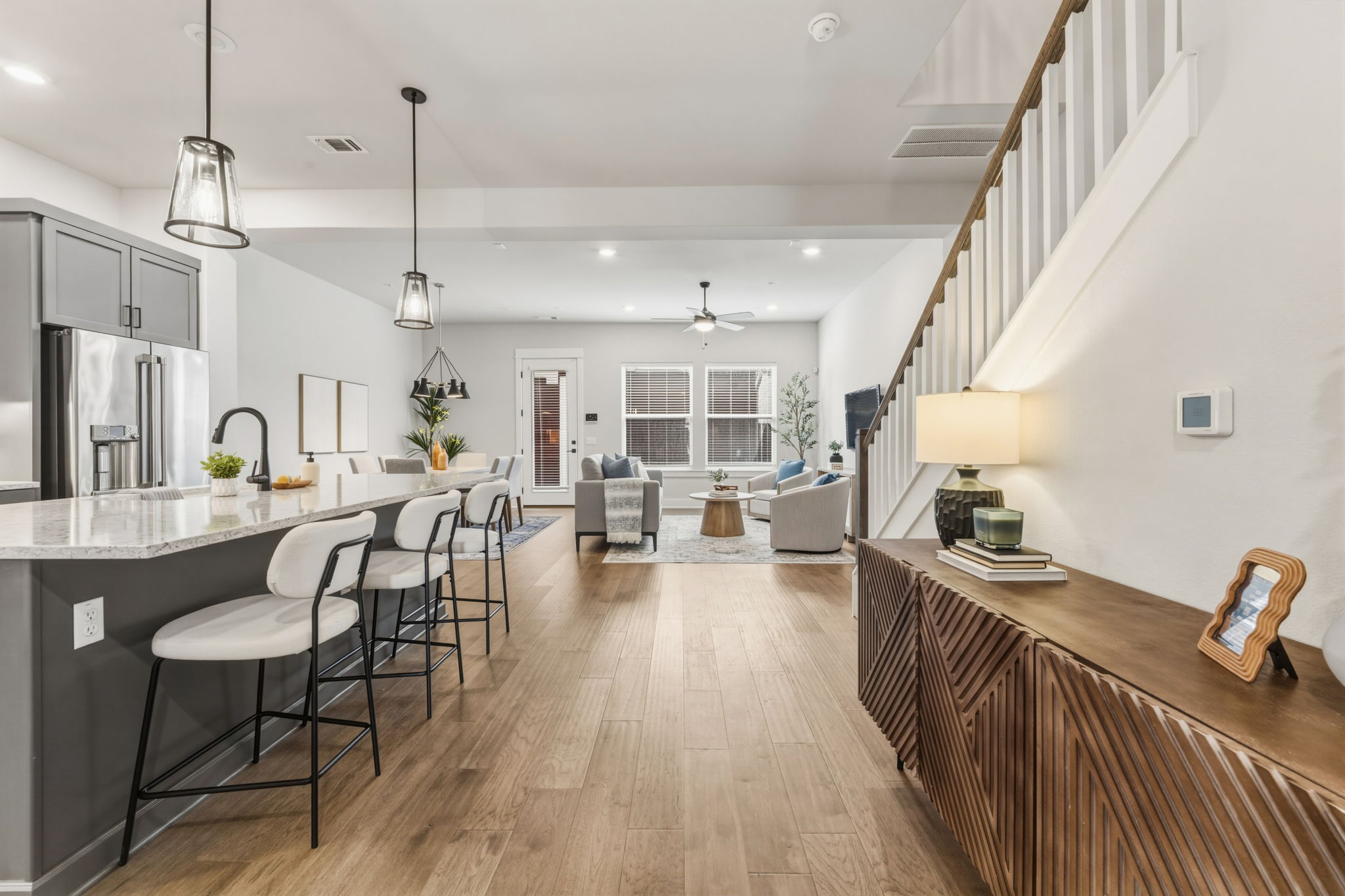 2929 Moreno Street Austin, TX 78723 - Photo 8 of 40 Open-concept living area featuring wood-finish flooring throughout, a kitchen island with pendant lighting, gray cabinetry, stainless steel appliances, and a staircase with white balusters