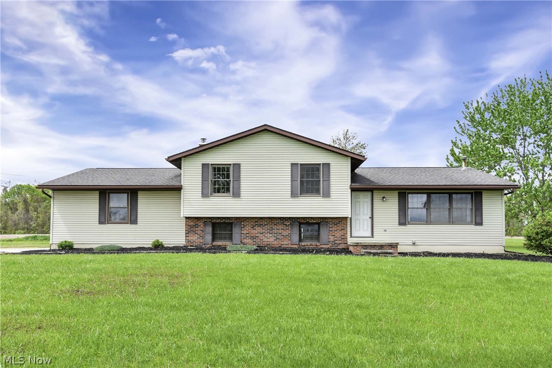 Split-level, featuring light/cream-colored siding, contrasting dark brown shutters and roof, and exposed brick