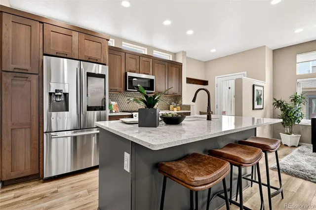 a kitchen with stainless steel appliances granite countertop a refrigerator a sink a stove and chairs with wooden floor