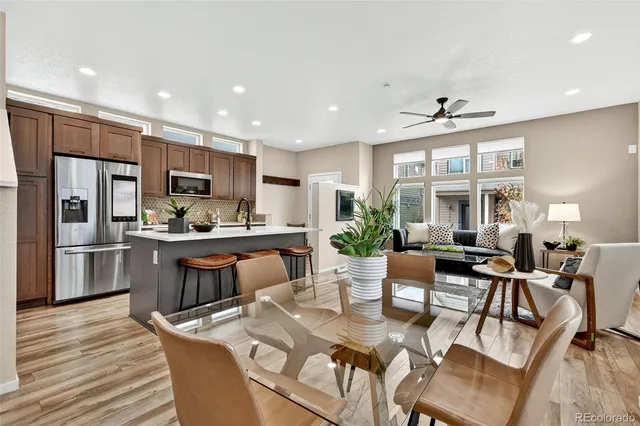 a kitchen with stainless steel appliances kitchen island granite countertop a refrigerator a stove a sink a dining table and chairs with wooden floor