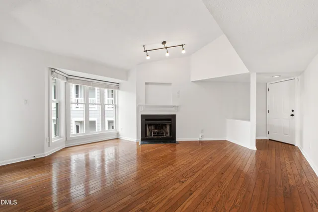 an empty room with wooden floor fireplace and windows