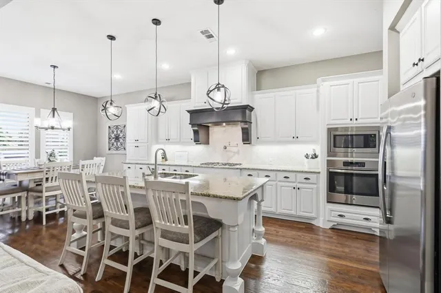 a kitchen with stainless steel appliances granite countertop a stove a refrigerator a oven a white with a dining table and chairs with wooden floor