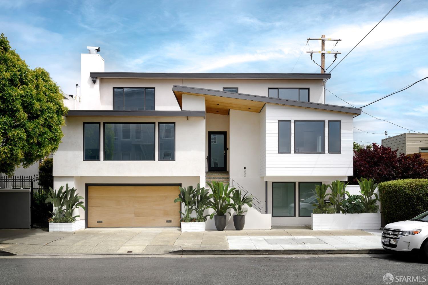 a view of a white house with potted plants and large tree