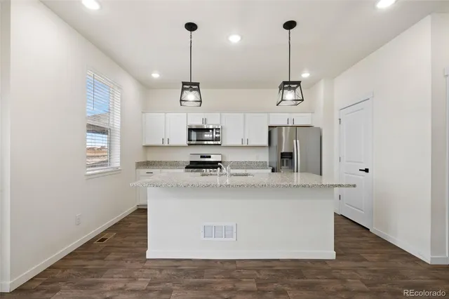 a view of kitchen with stainless steel appliances granite countertop a sink a stove a refrigerator and white cabinets