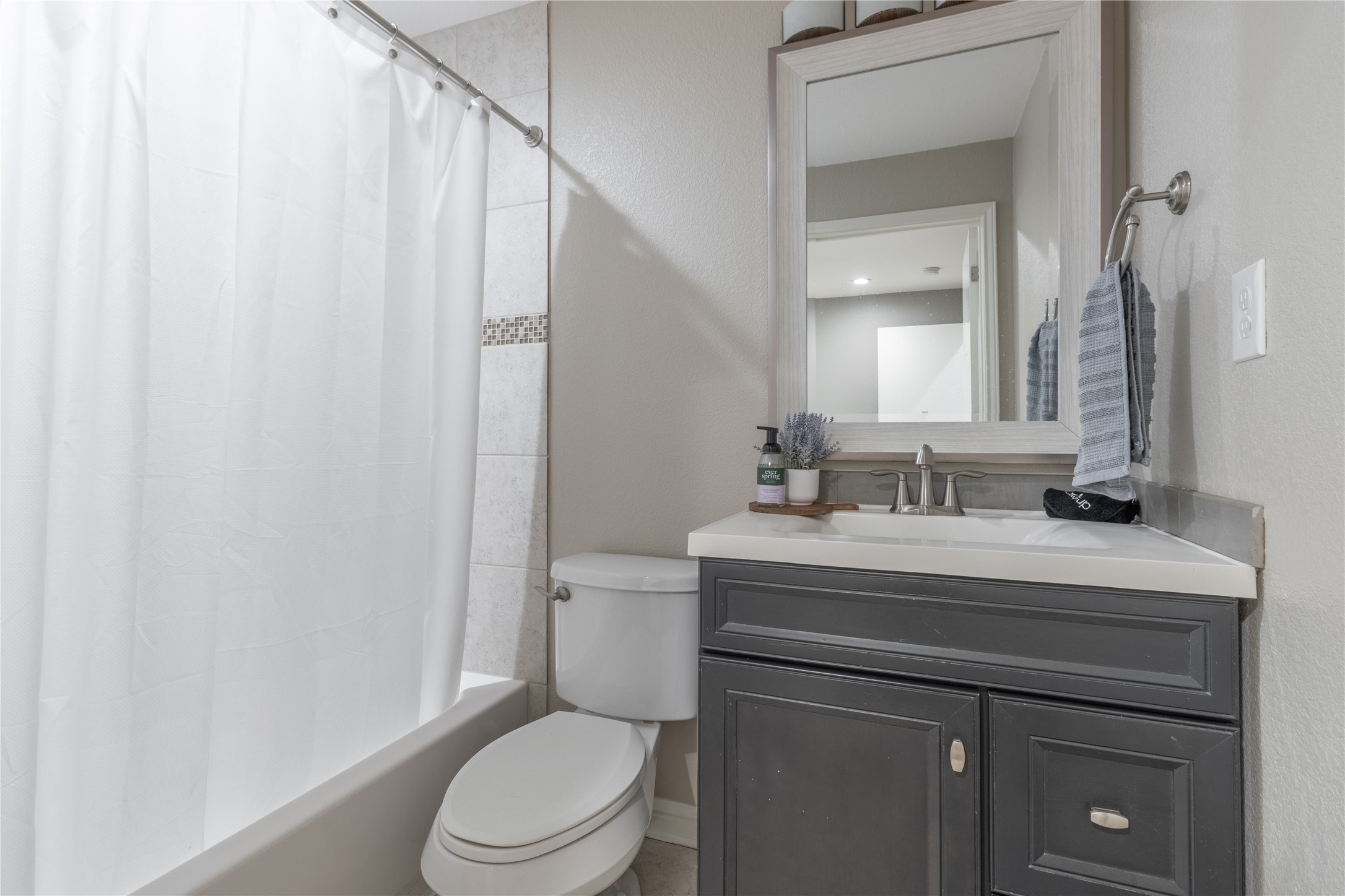 17123 Atlanta Street Humble, TX 77396 - Photo 14 of 29 This bathroom features a modern design with a sleek vanity, framed mirror, and neutral tones. It includes a combination shower and bathtub with a simple white curtain, creating a clean and inviting space.