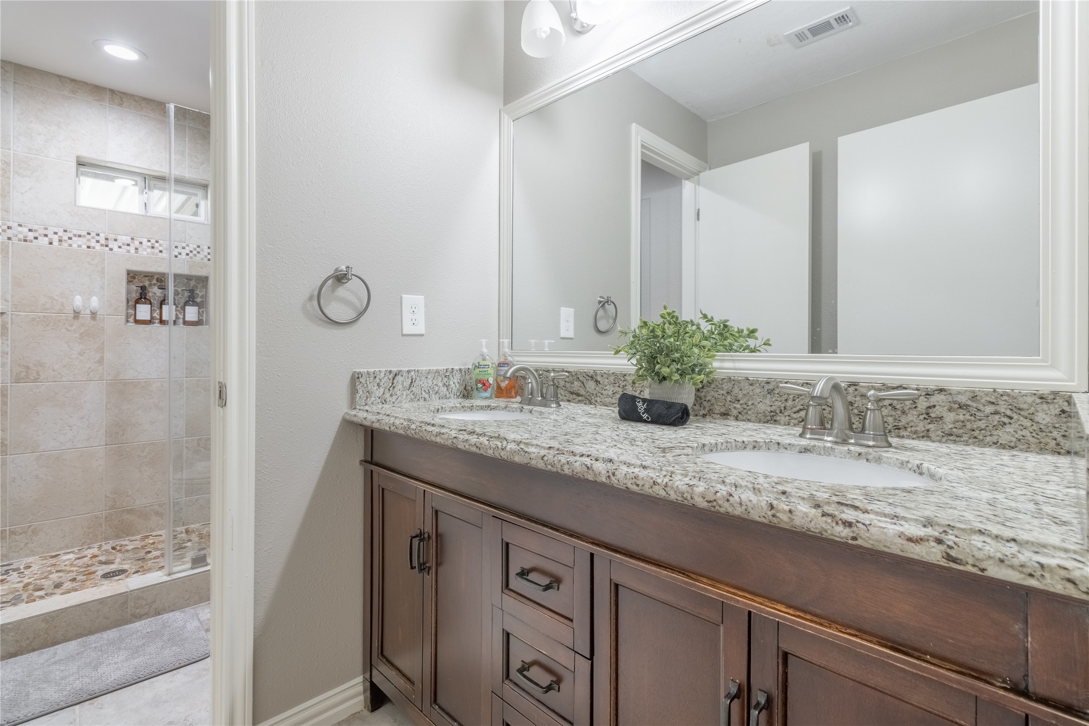 17123 Atlanta Street Humble, TX 77396 - Photo 15 of 29 This bathroom features a sleek granite countertop with a dual-sink vanity and elegant cabinetry. It includes a spacious walk-in shower with glass doors and tasteful tile work, creating a modern and inviting space.
