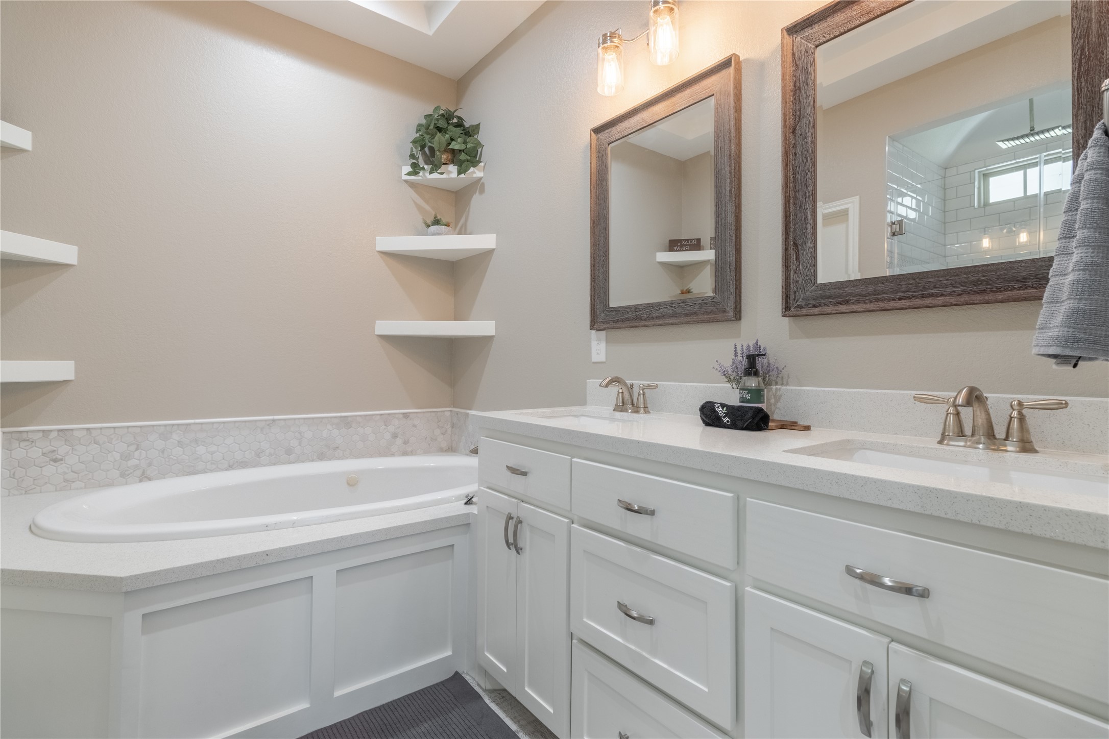 17123 Atlanta Street Humble, TX 77396 - Photo 21 of 29 This bathroom features a clean, modern design with dual sinks, elegant mirrors, and ample storage in white cabinetry. A corner bathtub with surrounding tile accents adds a touch of luxury.