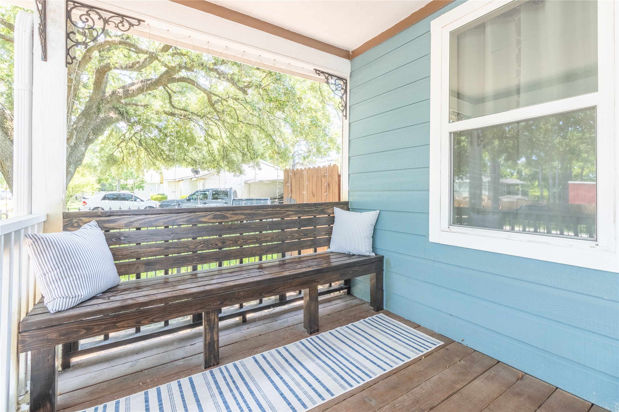 17123 Atlanta Street Humble, TX 77396 - Photo 3 of 29 Charming front porch with a wooden bench, accent pillows, and a cozy rug. It features a blue exterior wall and decorative trim, perfect for relaxing under the shade of nearby trees.