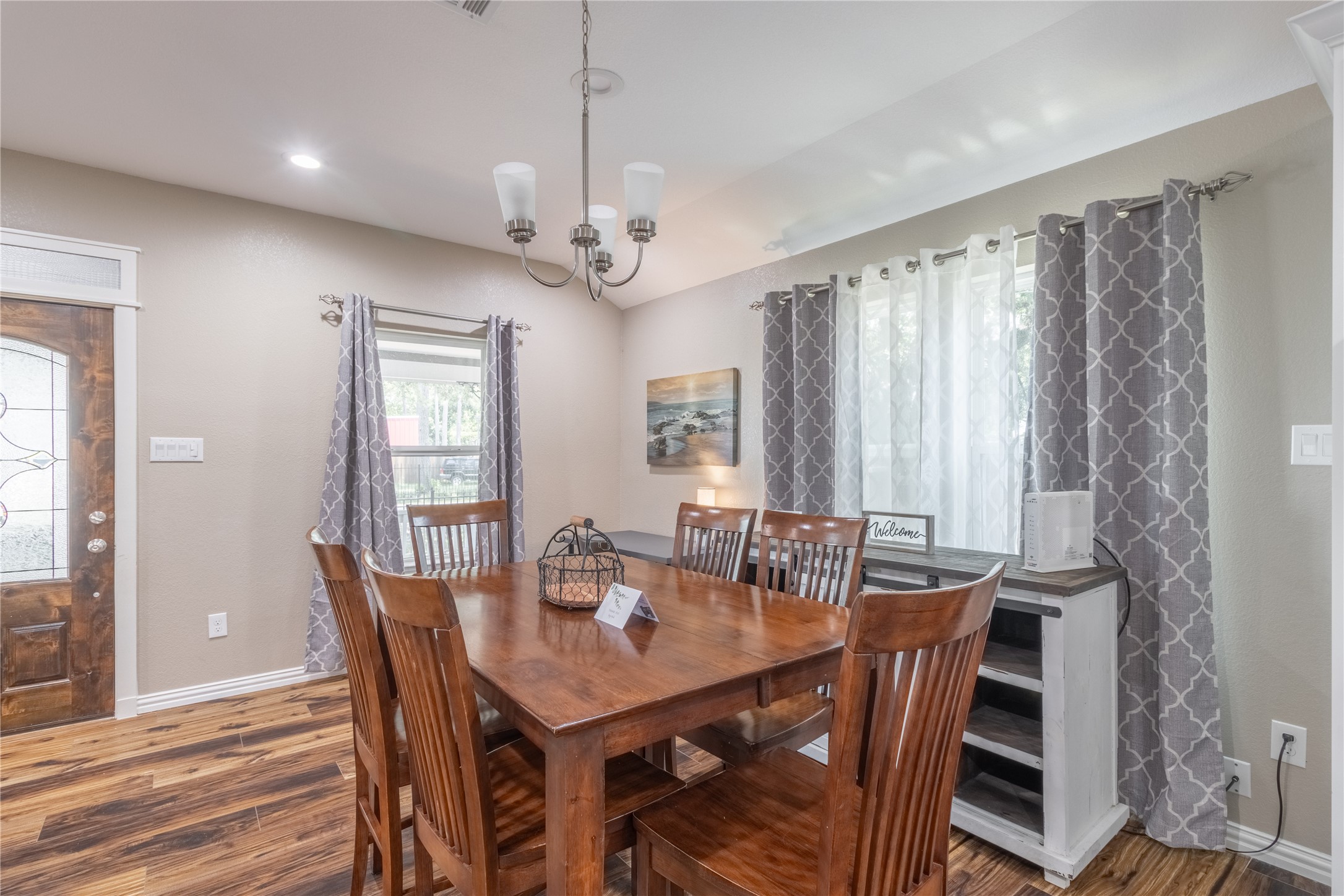 17123 Atlanta Street Humble, TX 77396 - Photo 6 of 29 This dining area features a warm, inviting atmosphere with a wooden table and chairs, complemented by hardwood floors. Natural light streams through large windows with patterned curtains, and a chandelier adds elegance. The space is cozy and welcoming, ideal for family gatherings.
