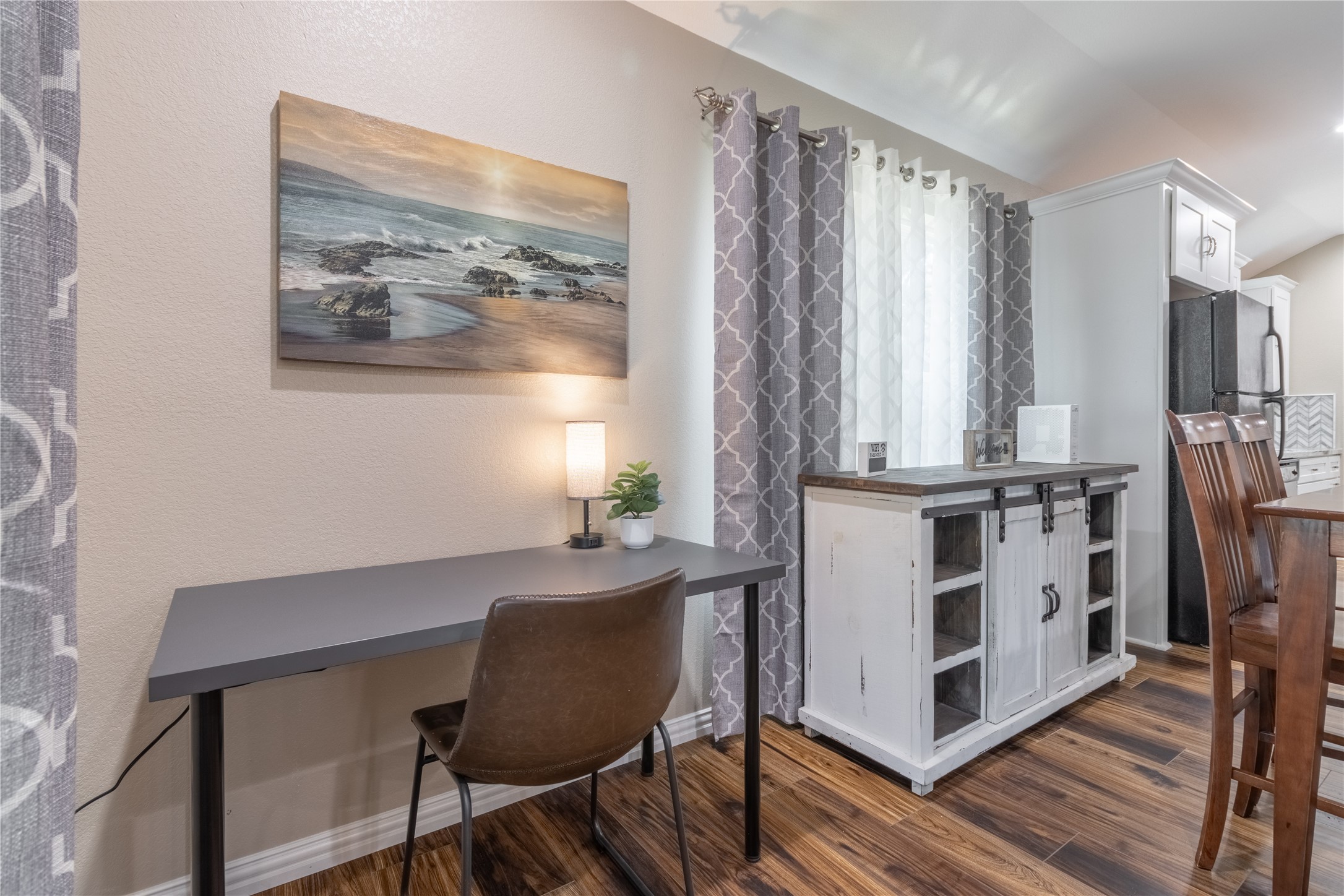 17123 Atlanta Street Humble, TX 77396 - Photo 7 of 29 This cozy corner features a small workspace with a sleek desk and chair, complemented by a stylish sideboard and dining area. The room is brightened by a large window with elegant curtains, wood flooring, and tasteful wall art.