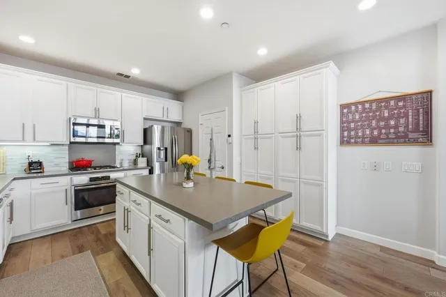 a kitchen with kitchen island a stove a sink a refrigerator white cabinets and wooden floor