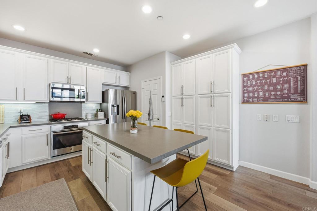 6485 Alexandri Circle Carlsbad, CA 92011 - Photo 6 of 40 a kitchen with kitchen island a stove a sink a refrigerator white cabinets and wooden floor