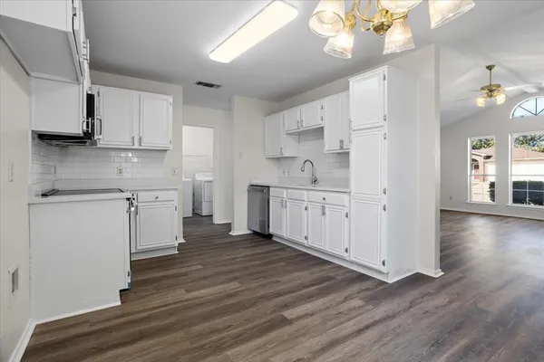 a kitchen with stainless steel appliances granite countertop a dishwasher a stove and white cabinets with wooden floor