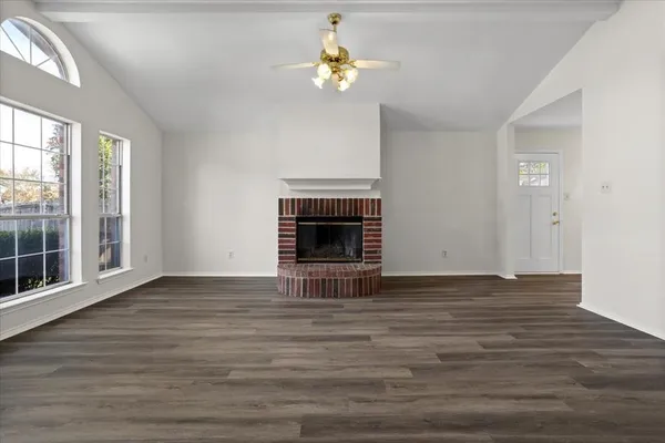 a view of an empty room with wooden floor fireplace and a window